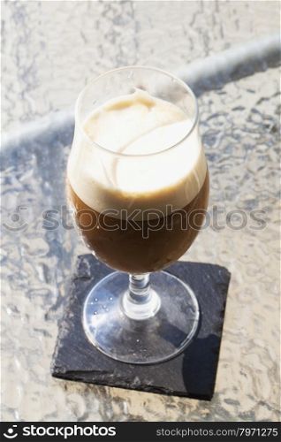 Foamy cocktail in glass over outdoor table, vertical image
