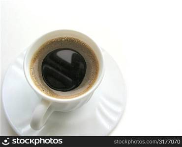 Foamy espresso coffee in a white cup with saucer on white background, top view, space for copy