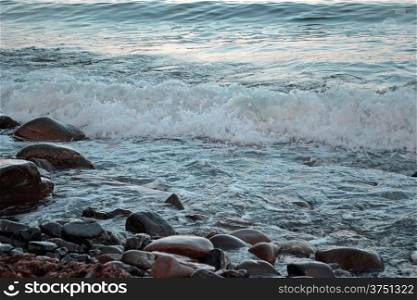 Foamy wave on the stone seashore at sunset