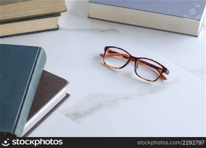 Focus at eyeglasses with various textbooks stack on white marble table