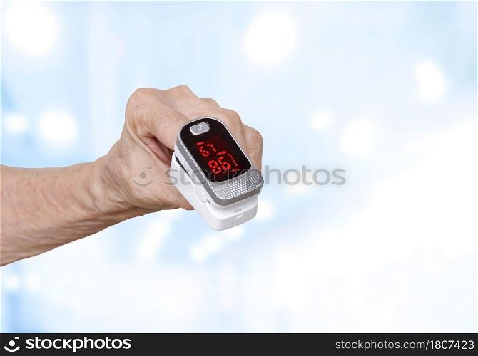 Focus at Pulse oximeter on the index finger of elderly hand with blurred hospital room background
