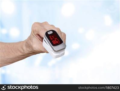 Focus at Pulse oximeter on the index finger of elderly hand with blurred hospital room background