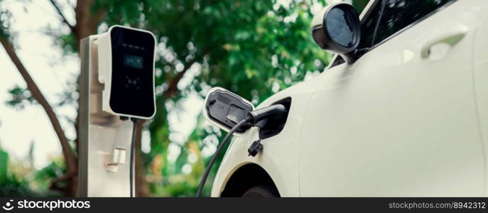 Focus closeup electric vehicle plugged in with EV charger device from blurred background of public charging station powered by renewable clean energy for progressive eco-friendly car concept.. Focus closeup EV car and charger with blur background for progressive concept