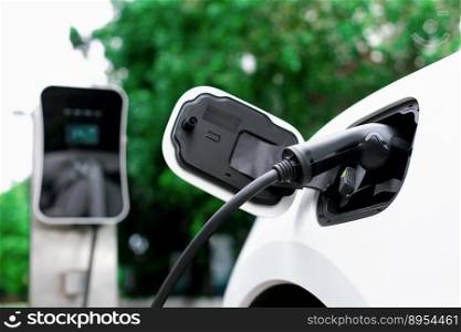 Focus closeup electric vehicle plugged in with EV charger device from blurred background of public charging station powered by renewable clean energy for progressive eco-friendly car concept.. Focus closeup EV car and charger with blur background for progressive concept