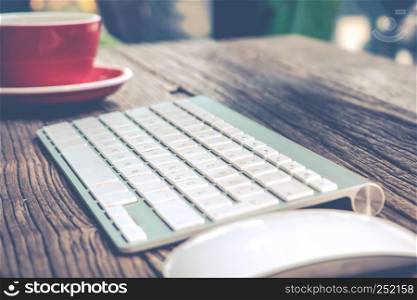 focus on English alphabet of the while keyboard with mouse and red cup of coffee