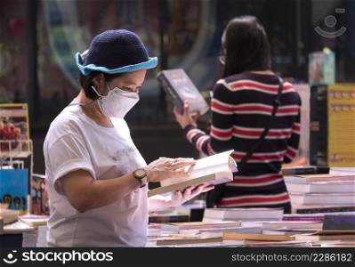 Focus on foreground at Asian plus size woman in protective face mask choosing books at bookstore in shopping mall area