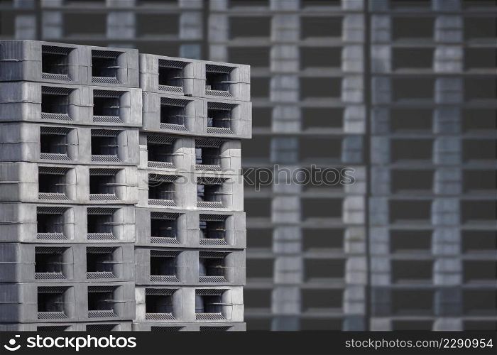 Focus on foreground at stack of many plastic shipping pallets outside of warehouse building
