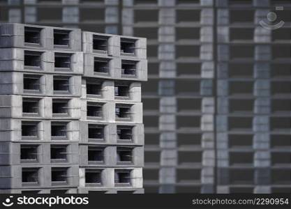 Focus on foreground at stack of many plastic shipping pallets outside of warehouse building