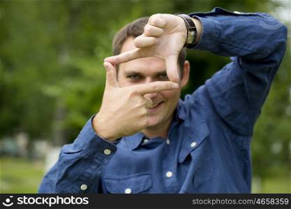 Focus on hand. A man looking and focusing through his hands, on green summer background