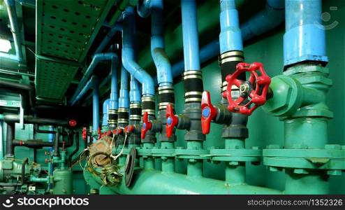 Focus on red gate valve on foreground with pipelines of main water pressure control in engine room area of fishing vessel