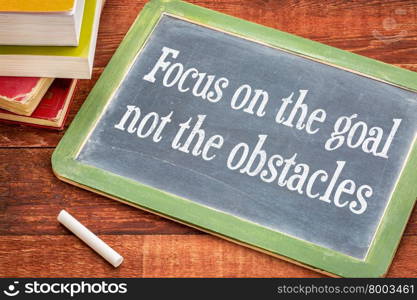 Focus on the goal, not the obstacles - inspirational advice on a slate blackboard with a white chalk and a stack of books against rustic wooden table