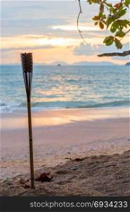 focus on the torch on the sandy beach of Thailand and the sunset on the sea