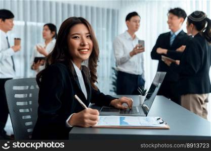 Focus portrait of female manger, businesswoman in the harmony meeting room with blurred of colleagues working together, analyzing financial paper report and dashboard data in background.. Focus portrait of asian female manger with blurred colleague figures in harmony.