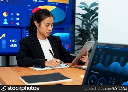 Focus portrait of female manger, businesswoman in the harmony meeting room with blurred of colleagues working together, analyzing financial paper report and dashboard data on screen in background.. Focus portrait of asian female manger with blurred background in harmony.
