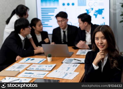 Focus portrait of female manger, businesswoman in the harmony meeting room with blurred of colleagues working together, analyzing financial paper report and dashboard data on screen in background.. Focus portrait of asian female manger with blurred background in harmony.