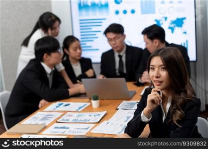 Focus portrait of female manger, businesswoman in the harmony meeting room with blurred of colleagues working together, analyzing financial paper report and dashboard data on screen in background.. Focus portrait of asian female manger with blurred background in harmony.
