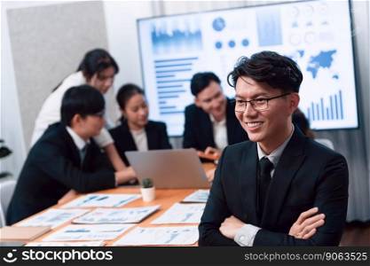 Focus portrait of successful confident male manager or executive in business wear with blurred background of businesspeople, colleagues working with financial report papers in office of harmony.. Focus portrait male manager in harmony office with businesspeople in background.