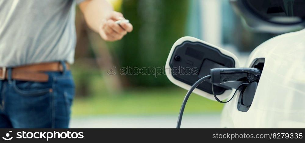 Focus recharging electric vehicle outdoor from charging station with blurred background of man at EV car. Concept ideal for new progressive technology of green and renewable energy for car.. Focus charging EV car with blurred background of man standing at progressive EV.