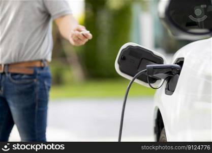 Focus recharging electric vehicle outdoor from charging station with blurred background of man at EV car. Concept ideal for new progressive technology of green and renewable energy for car.. Focus charging EV car with blurred background of man standing at progressive EV.