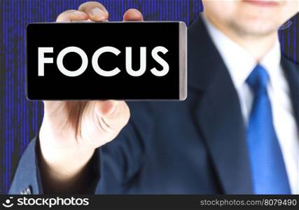FOCUS word on mobile phone screen in blurred young businessman hand and digital technology background, business concept