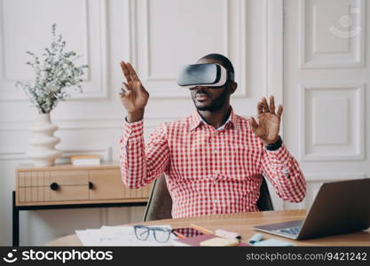 Focused Afro American businessman, VR headset on, immersed in virtual reality game  gesturing, interacting with cyber world objects.