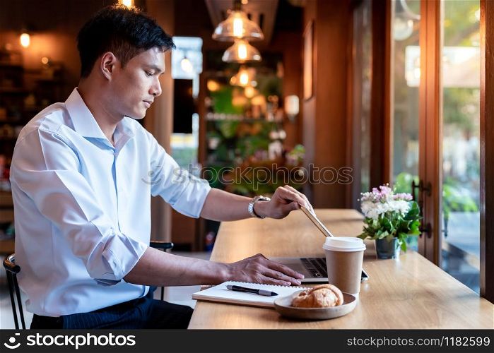Focused asian college student shut down his laptop in cafe.