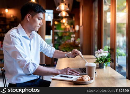 Focused asian college student shut down his laptop in cafe.