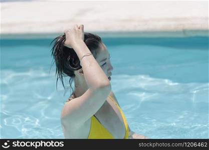 Focused beautiful asian woman in the pool holds her wet hair and looks ahead on an out of focus background. Leisure concept.. Asian woman in the pool holding her hair