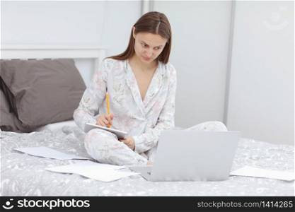 focused beautiful Business woman working on a laptop on the bed. girl studing at home office in quarantine. Stay at home. Freelance. Communication and technology concept. Coronavirus.. focused beautiful Business woman working on a laptop on the bed. girl studing at home office in quarantine. Stay at home. Freelance. Communication and technology concept. Coronavirus