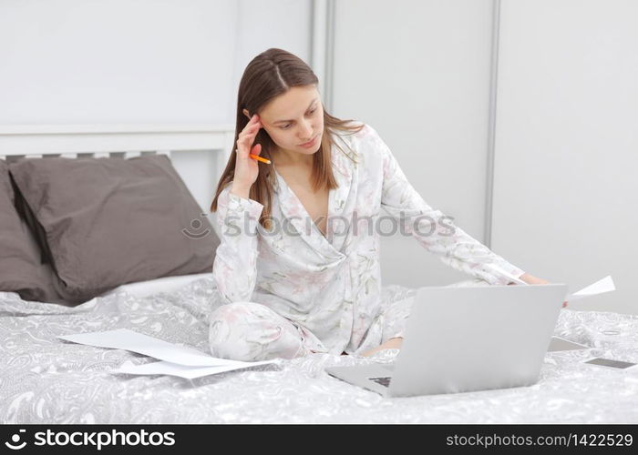 focused beautiful Business woman working on a laptop on the bed. girl studing at home office in quarantine. Stay at home. Freelance. Communication and technology concept. Coronavirus.. focused beautiful Business woman working on a laptop on the bed. girl studing at home office in quarantine. Stay at home. Freelance. Communication and technology concept. Coronavirus