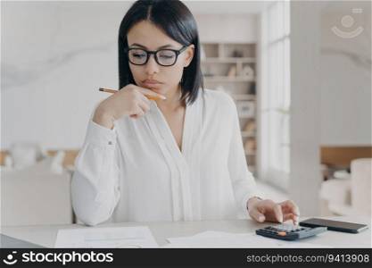 Focused businesswoman analyzes budget, calculates profit with calculator. Manager works on documents at office desk, handles expenses. Financial management.