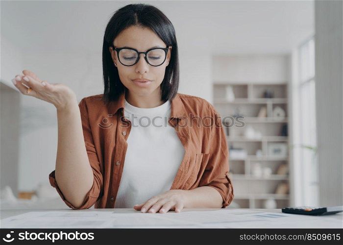 Focused female in glasses working with financial documents at home. Businesswoman calculating expenses, planning household budget for economy saving money, sitting at desk.. Female wearing glasses calculating expenses, planning household budget for saving money at home