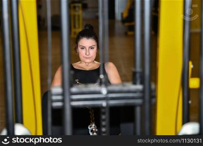 Focused looking woman uses a leg adductor machine at a gym with an out of focus foreground and background. Fitness concept.. Woman focuses using a leg adductor machine