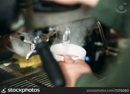 Focused male hands with white cup and blured coffee machine.