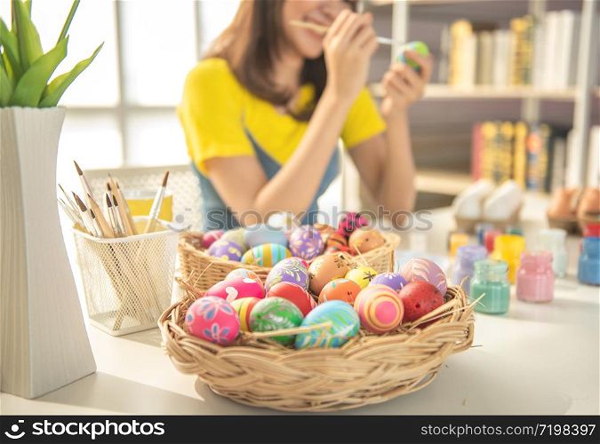 Focused on basket of decorated easter eggs with blurred of beautiful young asian woman painting easter eggs on table with decorated eggs for celebrate April Easter day with copy space.
