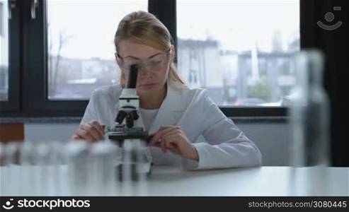Focused scientists in protective goggles and lab coat working with microscopes and making research in laboratory. Concentrated scientific researchers looking at biological samples under microscope and conducting an experiment in lab. Dolly shot.