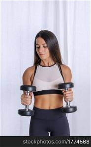 Focused sportswoman in activewear doing exercises with dumbbells while training in room at home. Fit woman exercising with dumbbells at home