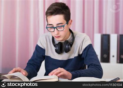 Focused teenage boy reads a book while sitting at a table in an out of focus background. Student concept.. Focused looking teenage boy studies a book