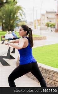 Focused young woman wearing tights and a tank top stretching at a park on an out of focus background. Healthy lifestyle concept.