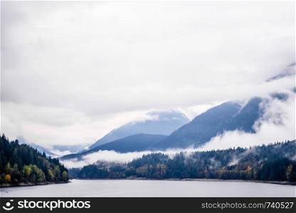 Fog and clouds covering forested mountains near lake in British Columbia, Canada.