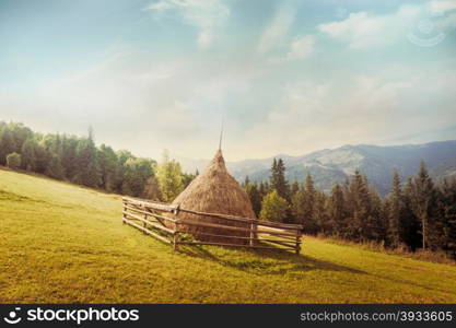 Foggy sunny morning landscape with hay stack on meadow at highland Carpathian mountains. Green tourism