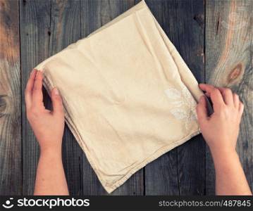 folded beige textile kitchen towel and two hands on a gray wooden background, top view