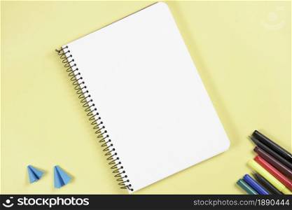 folded craft paper felt tip pen near blank spiral notepad yellow background