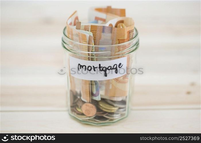 folded euro notes coins mortgage glass jar wooden backdrop
