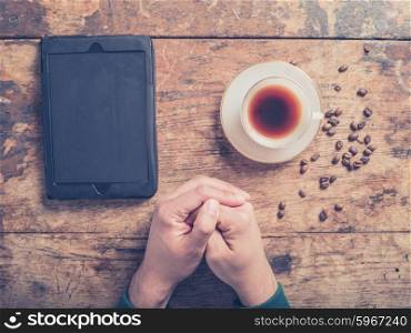 Folded male hands on a wooden table with a tablet computer, cup of coffee and beans