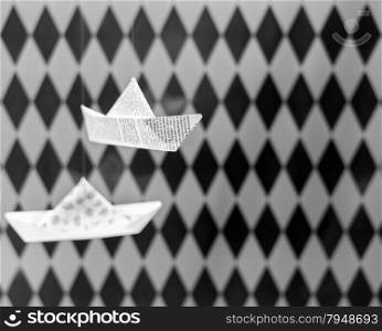 Folded Origami Paper Boats suspended in front of Diamond Checkered Background