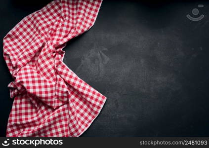 Folded red and white cotton kitchen napkin on a wooden black background, top view, copy space