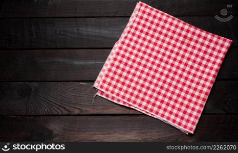 folded red and white cotton kitchen napkin on a wooden brown background, top view, copy space
