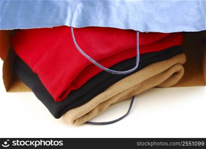 Folded sweaters in a paper shopping bag on white background