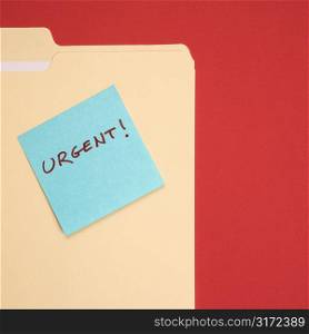 Folder with a blue sticky note attached reading urgent on a red background.